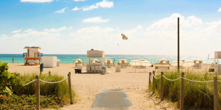 gray pathway leading to parasol, lifeguard house, and sea a daytime