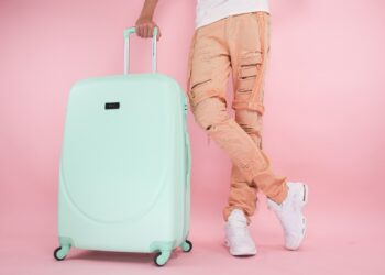 Person Wearing Brown Pants Standing beside a Green Suitcase