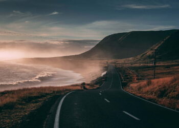 black road besides seashore and mountain at sunset