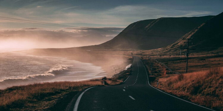 black road besides seashore and mountain at sunset