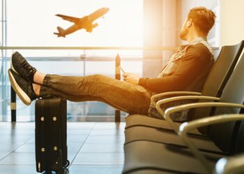 man sitting on gang chair with feet on luggage looking at airplane