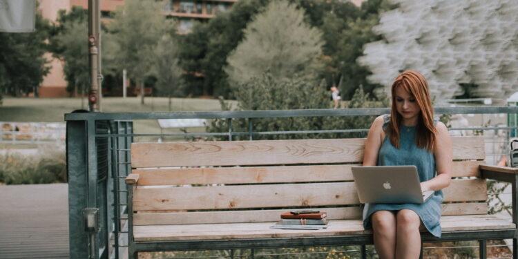 woman sitting on bench white using MacBook Pro