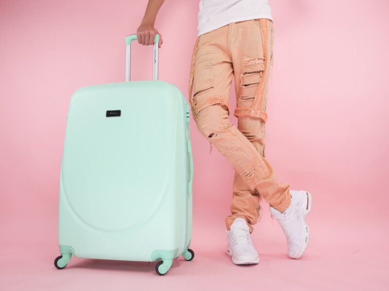 Person Wearing Brown Pants Standing beside a Green Suitcase